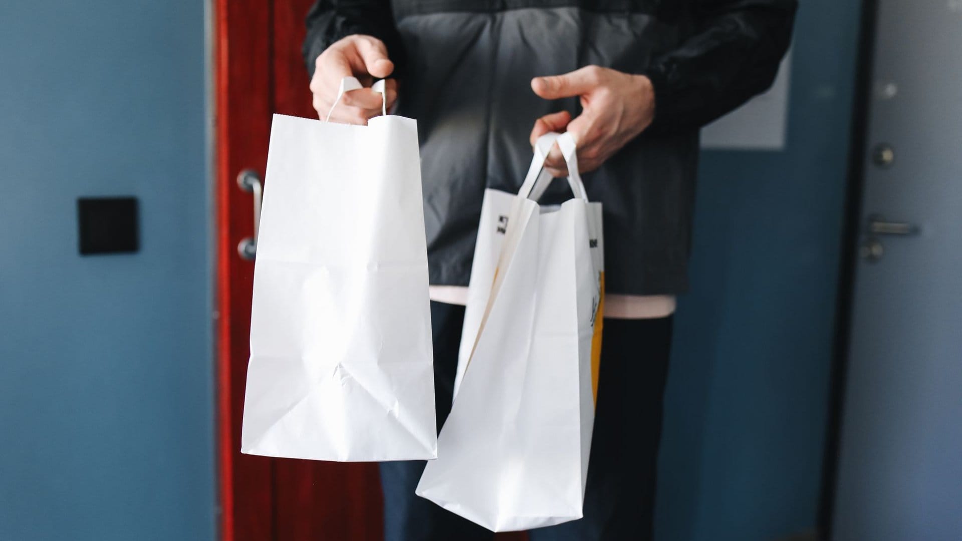 Person übergibt weiße Apotheken-Papiertüten an der Haustür – Sinnbild für den rezeptfreien Kauf und Versand von Klysmen