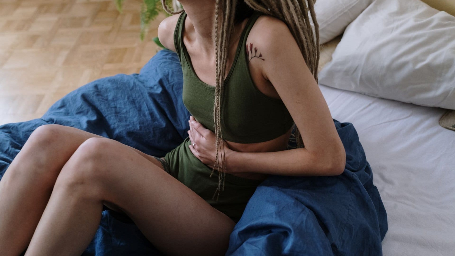 Frau sitzt auf dem Bett und hält sich mit beiden Händen den Bauch, wartend