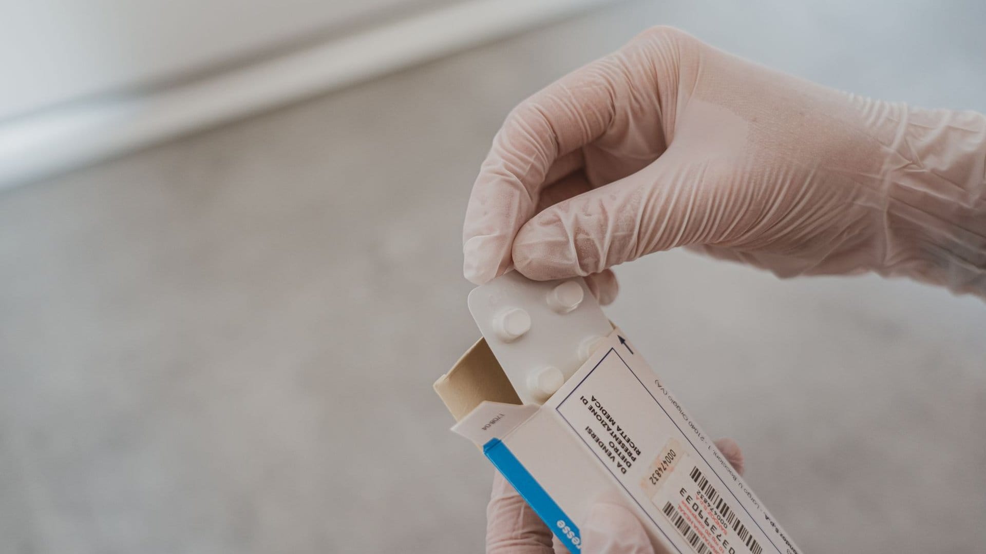 Hand mit Einweghandschuh öffnet eine Medikamentenpackung mit Tablettenblister als Symbolbild für apothekenpflichtige, rezeptfreie Arzneimittel